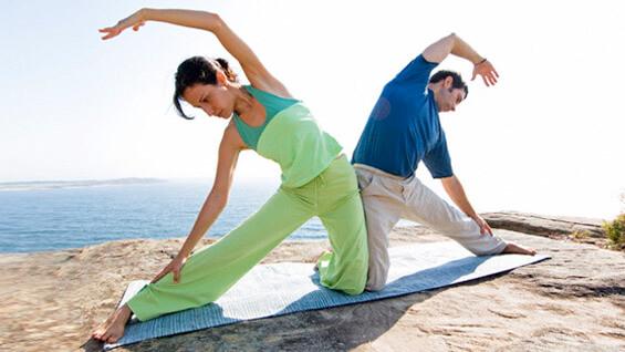 A man and woman practicing yoga on a rocky outcrop above the Pacific Ocean