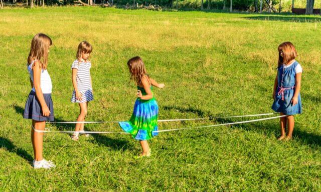 Four little girls are playing elastics in the park